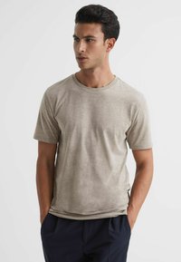 Tricou cu gât rotund de culoare bej deschis, realizat dintr-un material moale; mâneci scurte și o croială relaxată, cu o suprafață netedă, ușor texturată.