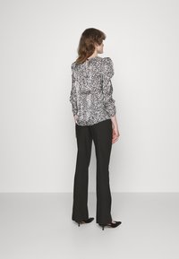 Blusa preta e branca com padrões, com mangas bufantes, combinada com calças pretas de boca de sino. Modelo vista de costas, usando sapatos de salto pretos elegantes.