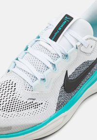 Scarpa sportiva bianca con tomaia in rete, logo Swoosh nero e dettagli turchesi sulla suola. Caratterizzata da sovrapposizioni testurizzate e lacci bianchi.