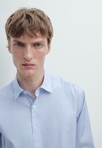 Camicia azzurra a righe con colletto aperto e bottoni bianchi, realizzata in tessuto di cotone, con una texture morbida e una vestibilità attillata.