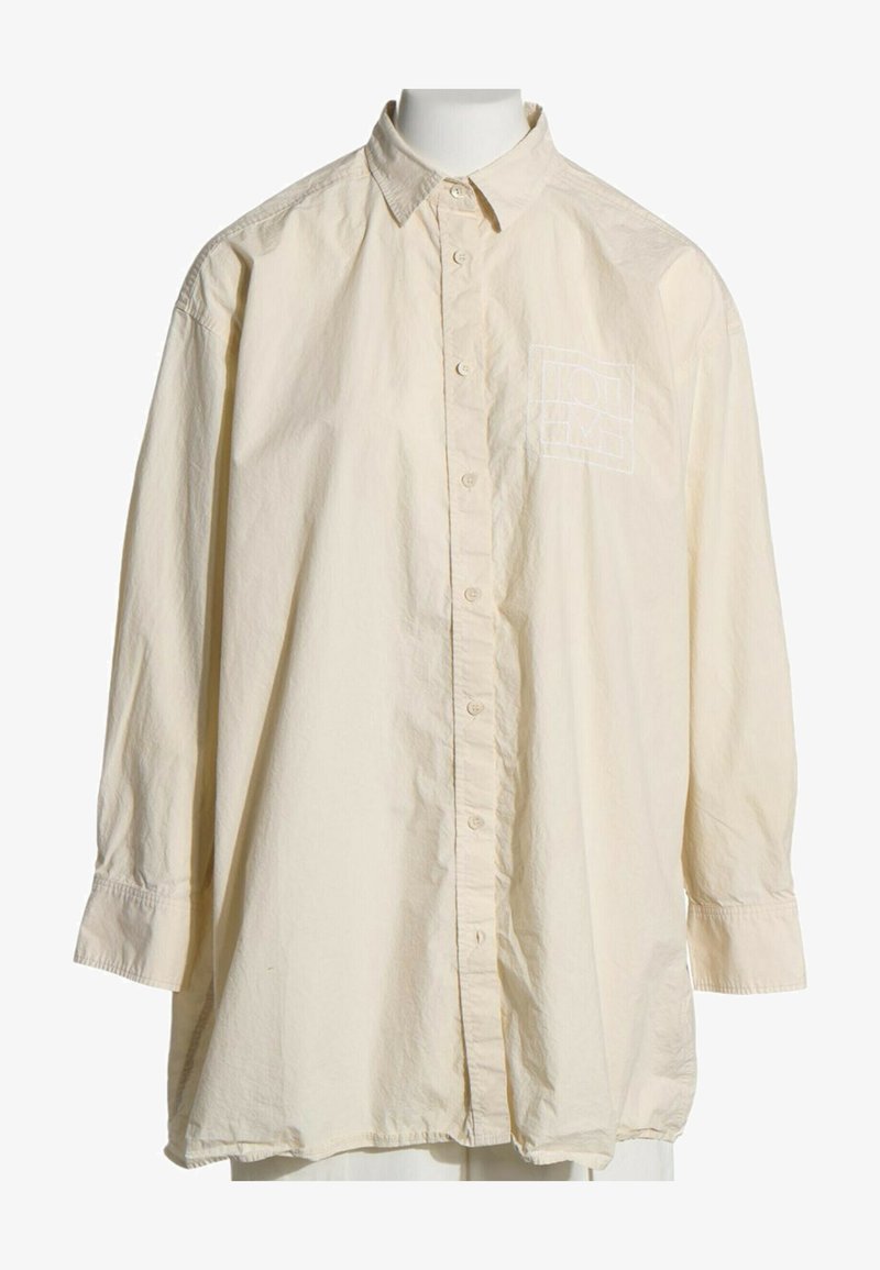 Chemise beige à manches longues avec boutons, col, coupe ample et un subtil logo carré brodé sur la poitrine gauche.