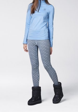 Helles blaues Langarmoberteil, gemusterte Leggings mit weißem und marineblauem geometrischem Design sowie schwarze gesteppte Stiefel mit Pelzkragen.
