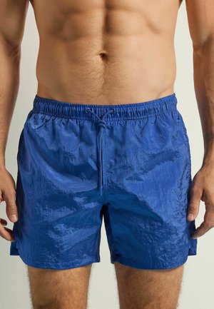 Blaue Schwimmshorts mit einer strukturierten, glänzenden Oberfläche. Elastischer Taillenbund mit Kordelzug. Verfügt über seitliche Schlitze für Bewegungsfreiheit und eine lockere Passform.