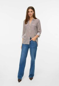 Chemise à rayures à boutons avec deux poches poitrine, manches longues retroussées aux poignets, associée à un jean bleu à jambes larges et des chaussures marron à bout pointu.