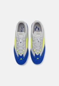 Scarpe sportive con una tomaia in mesh grigia, dettagli in suede blu e strisce giallo neon. Presentano lacci grigi e una suola testurizzata per una buona aderenza.