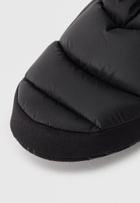 Chaussure noire rembourrée avec une tige texturée et une semelle en caoutchouc noir solide. Présente une finition lisse et un design matelassé pour l'isolation.