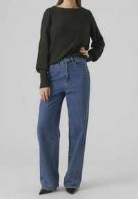 Maglione nero a maglia testurizzata con scollo ampio, abbinato a jeans blu a vita alta e gamba dritta, e tacchi neri a punta.