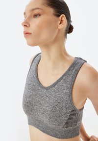 Grå sportsbh med scoop-udskæring, blødt stof og et tekstureret mønster på siden. Den har en tætsiddende design og brede stropper.