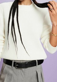 Maglione a coste di colore crema con maniche ampia, abbinato a pantaloni grigi a vita alta con pieghe e una cintura in pelle nera con fibbia argentata.