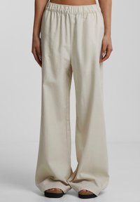 Ljust beige vida byxor gjorda av mjukt, strukturerat tyg med resårmidja, visade på en modell som bär svarta plattformssandaler.