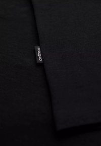 Tissu noir, texture lisse, deux couches superposées, avec une petite étiquette de marque dans un coin comportant le texte "ontbre".