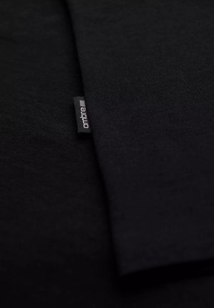 Mustaa kangasta, sileä pinta, kaksi kerrosta päällekkäin, kulmassa pieni tuotemerkki, jossa on teksti "ontbre".