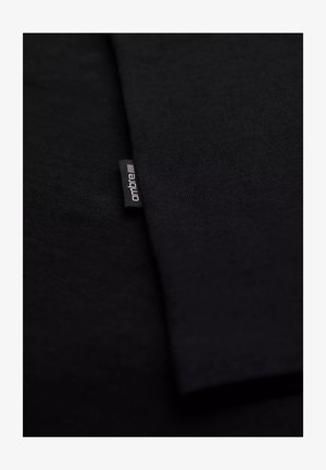 Schwarzer Stoff, glatte Textur, zwei überlappende Schichten mit einem kleinen Markenschild in der Ecke, auf dem der Text "ontbre" steht.