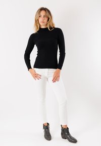 Top nero a coste con maniche lunghe e collo alto, con dettagli testurizzati, abbinato a pantaloni skinny bianchi e stivaletti neri.