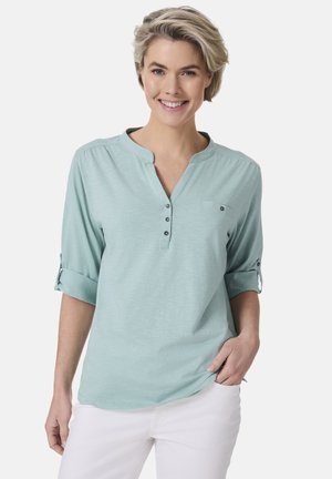 Hellblaues Blusenshirt mit Stehkragen, Knopfleiste, hochkrempelbaren Ärmeln und einer kleinen Brusttasche. Weicher, strukturiertes Material.