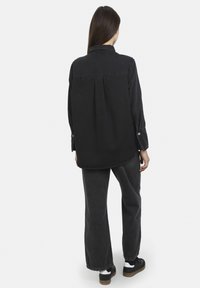 Camicia nera a maniche lunghe con colletto a bottoni e piega sul retro, abbinata a jeans dritti grigio scuro e sneakers nere.