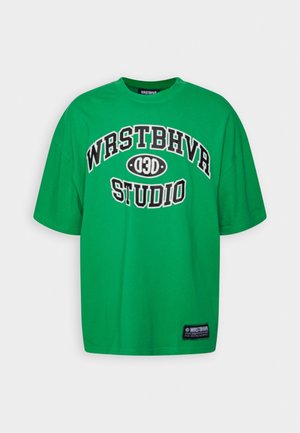 Zielony t-shirt z krótkim rękawem z czarnym i białym tekstem "WRSTBHVR 030 STUDIO" z przodu oraz małą czarną metką przy dolnym brzegu.