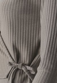 Gray ribbed top with a fitted design, featuring a tie at the waist and soft texture, highlighting vertical lines and elastic material.