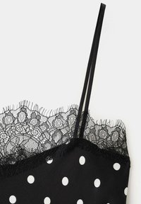 Top noir à fines bretelles avec des pois blancs et une délicate bordure en dentelle noire le long de l'encolure.