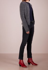 Grå, stickad kofta med långa ärmar och rund hals, bärs över en marinblå topp. Kombination med svarta jeans och röda, spetsiga ankelstövlar.