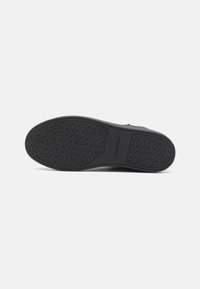 Semelle de chaussure en caoutchouc noir avec motif texturé, arborant la marque Calvin Klein. Forme plate et ronde avec une finition lisse. Conçue pour l'adhérence et la durabilité.