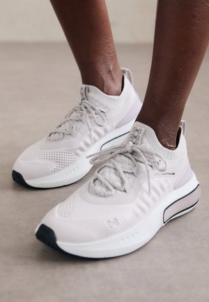 Helle graue Sportschuhe mit einem strukturierten Strick-Obermaterial, gepolsterter Sohle und schwarzen Akzenten, die für Komfort und Leistung konzipiert sind.