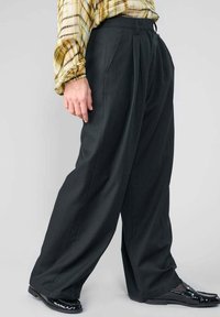 Schwarz pleated Weite Hosen mit vertikalen Streifen, hoher Taille und Seitentaschen, kombiniert mit glänzenden schwarzen Schuhen.
