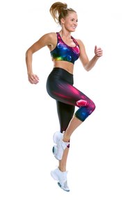 Sportovní podprsenka s mnohobarevným geometrickým vzorem, doplněná černými 3/4 legínami se živými akcenty a bílými sportovními botami.