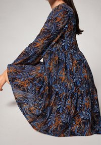 Robe à manches longues avec un fond noir, ornée d'un motif floral aux teintes bleues et orange, design à volants et texture de tissu fluide.