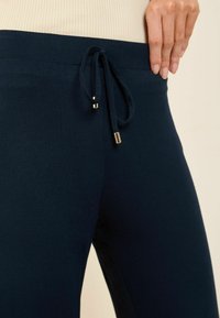 Pantalons navy à cordon de serrage fabriqués dans un tissu doux, dotés d'une large ceinture et de pointes dorées sur les cordons ajustables.