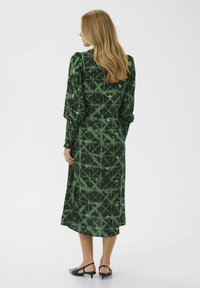 Roheline kleit mustriga tekstuuriga, millel on kullatud aktsendid ja puhvis varrukad. Disain sisaldab geomeetrilisi kujundeid ja keskmise pikkusega lõiget.