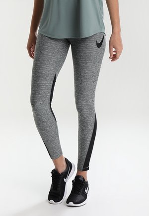 Leggings elasticizzati e aderenti di colore grigio con un motivo melange. Pannelli laterali neri e dettagli con il logo Nike. Abbinati a scarpe da ginnastica nere.