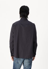 Button-up shirt in dark navy with thin vertical stripes in rust, featuring a pointed collar and buttoned cuffs, made from soft fabric.