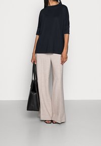 Mörk marinblå lös passform topp med uppvikta ärmar, i kombination med ljusbeige vida byxor. Svart väska, platta sandaler och släta texturer ingår.