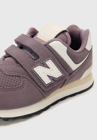 Violetti mokkasandaalit, joissa on valkoisia yksityiskohtia, tarranauhat, rei'itetty kärki ja musta kumipohja. Varustettu näkyvällä brändilogolla.