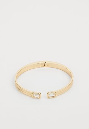 Bracciale rigido aperto in oro con due pietre preziose rettangolari trasparenti alle estremità e sottili dettagli incisi a linee.