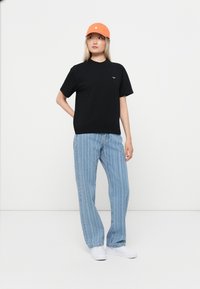 Black cotton t-shirt with a small logo, paired with light blue vertical striped jeans and an orange cap, finished with white shoes.