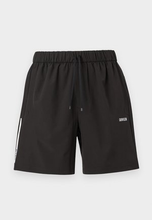 Zwarte shorts met elastische tailleband, trekkoord, zijzakken en wit Calvin Klein-logo op de rechterdij en een witte streep aan de linkervoet.