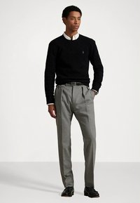 Μαύρο πουλόβερ πλεκτό με σχέδιο καλωδίου πάνω από λευκό πουκάμισο με γιακά, σετ με ανοιχτό γκρι παντελόνι με πιέτες και μαύρα δερμάτινα παπούτσια. Απλή, κομψή εμφάνιση.