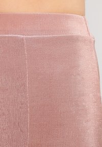 Lichtroze ribbelstof met een gladde textuur, voorzien van een hoge tailleband en verticale naadtoeslagen voor een nauwkeurige pasvorm.