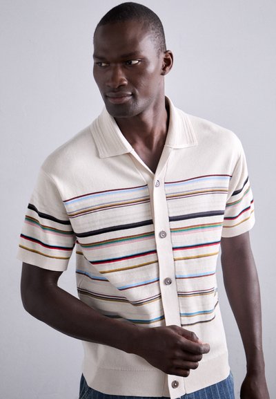 Korte mouw gebreide poloshirt in crèmekleur met meerkleurige horizontale strepen. Heeft een kraag en een sluiting met knopen aan de voorkant.