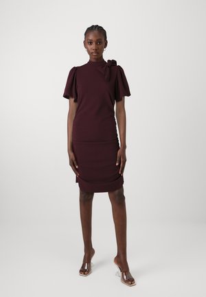 Burgundy mekko, jossa on lyhyet puffi-hihat, solmukohta olkapäällä ja sivuilla rypytys. Yhdistetty läpinäkyviin korkokenkiin.