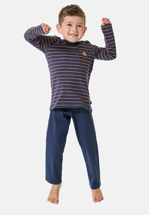 Marineblaues Langarmshirt mit orangefarbenen Streifen und einem kleinen Fuchs-Emblem, kombiniert mit marineblauen Hosen. Das Kind springt fröhlich und barfuß.