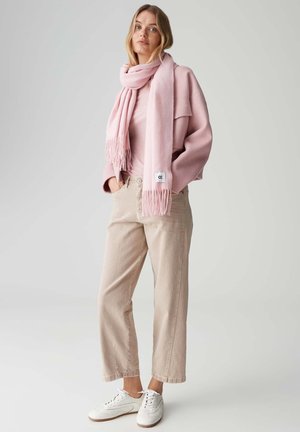 Roze oversized trui, bijpassende sjaal met franjes en beige wijde broek; witte sneakers met een minimalistisch design. Zachte, gestructureerde materialen.