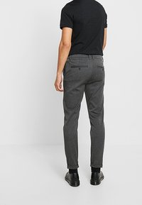 Grijze op maat gemaakte broek met een slim fit, met een gladde textuur, achterzakken en manchetogen, gecombineerd met een zwart shirt met korte mouwen.