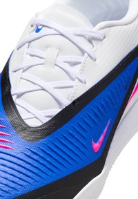 Κοντινό ενός αθλητικού παπουτσιού λευκού, μπλε και μαύρου χρώματος με λευκά κορδόνια και ένα μικρό ροζ σήμα Nike στο πλάι.