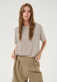 Pasiasty t-shirt w odcieniach beżu i kremu, okrągły dekolt, krótkie rękawy, luźny fason. W zestawie z beżowymi spodniami z wysokim stanem i plisami.