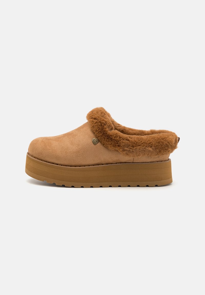 Chaussure marron à enfiler avec une semelle épaisse et une doublure douce et duveteuse autour de l'ouverture, ornée d'un petit pendentif en métal en forme de cœur sur le côté.