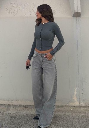 Grå långärmad skjorta med knappar, kombinerad med baggy ljusgrå jeans. Skjortan är kort och jeansen har hög midja och vida ben.