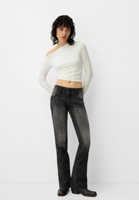 Crop top bianco off-shoulder abbinato a jeans dritti scuri leggermente sbiaditi, con cuciture a contrasto e tasche frontali.